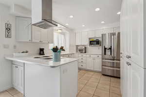 Kitchen with island range hood, stainless steel appliances, a peninsula, white cabinets, and light countertops