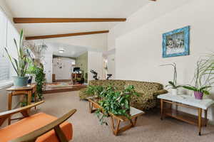 Carpeted living area with vaulted ceiling with beams