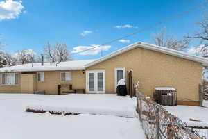 Snow covered back of property featuring fence, cooling unit, and stucco siding