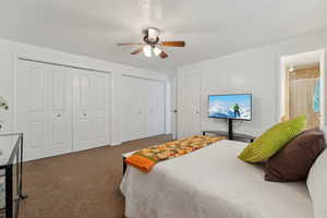 Bedroom with dark colored carpet, a ceiling fan, and multiple closets