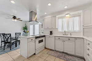 Kitchen featuring white appliances, island range hood, light countertops, white cabinetry, and a sink