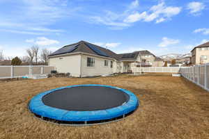 Back of house with solar panels, a yard, a trampoline, and a fenced backyard