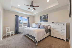 Carpeted bedroom featuring baseboards, a raised ceiling, a ceiling fan, and recessed lighting