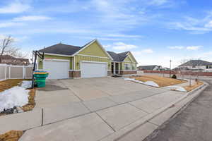 View of front facade featuring an attached garage, fence, driveway, stone siding, and board and batten siding