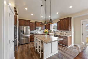 Kitchen with a center island, a breakfast bar, decorative light fixtures, stainless steel appliances, and light stone countertops