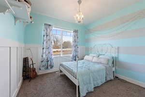 Bedroom with carpet floors, a chandelier, wainscoting, and a decorative wall