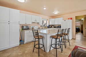 Kitchen featuring white appliances, white cabinets, a kitchen island, light countertops, and under cabinet range hood