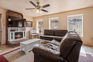 Living area featuring light tile patterned floors, a ceiling fan, a textured ceiling, and a glass covered fireplace