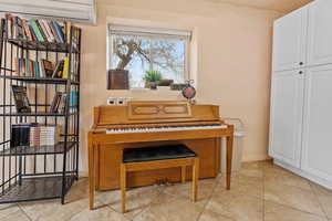 Living area with an AC wall unit, light tile patterned flooring, and baseboards