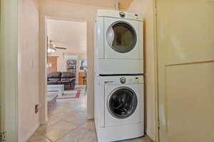 Laundry room featuring light tile patterned floors, stacked washer / drying machine, a ceiling fan, an AC wall unit, and laundry area