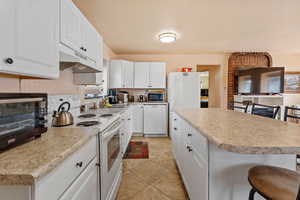 Kitchen featuring under cabinet range hood, white appliances, a breakfast bar, a kitchen island, and light countertops