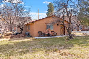 Rear view of property with brick siding, a lawn, and a patio