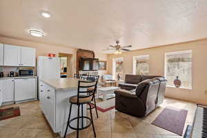 Kitchen featuring white appliances, open floor plan, a kitchen breakfast bar, light countertops, and white cabinetry