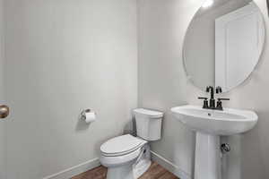 Half bath featuring toilet, baseboards, and wood finished floors