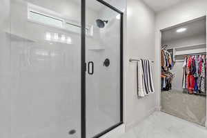 Bathroom with a stall shower, marble finish floor, a spacious closet, and baseboards