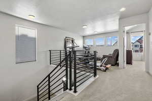 Exercise area with light carpet, baseboards, and a textured ceiling