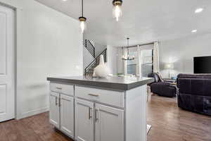 Kitchen featuring dark wood-type flooring, white cabinets, open floor plan, dark countertops, and decorative light fixtures