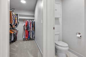 Bathroom featuring toilet, a spacious closet, and baseboards