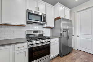 Kitchen with stainless steel appliances, dark countertops, white cabinetry, and wood finished floors