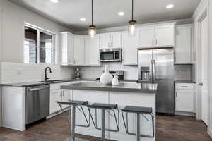 Kitchen featuring appliances with stainless steel finishes, dark countertops, white cabinets, and pendant lighting