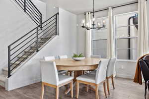 Dining space featuring light wood finished floors, baseboards, stairway, an inviting chandelier, and a textured ceiling