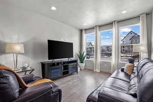 Living area with light wood-type flooring, a textured ceiling, baseboards, and recessed lighting