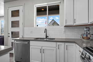 Kitchen featuring dishwasher, dark countertops, a sink, and white cabinetry