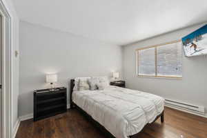 Bedroom with a baseboard heating unit, dark wood-style floors, and baseboards