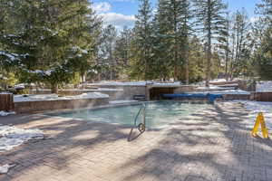 Snow covered pool featuring a patio area, a hot tub, and an outdoor pool