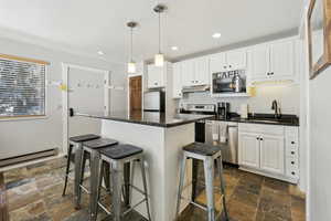 Kitchen featuring stainless steel appliances, dark countertops, a sink, and white cabinetry