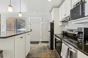 Kitchen featuring pendant lighting, stainless steel appliances, stone finish floor, white cabinetry, and under cabinet range hood