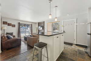 Kitchen featuring a breakfast bar area, dark countertops, hanging light fixtures, stone finish floor, and open floor plan