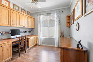 Home office with ornamental molding, ceiling fan, built in desk, and light wood finished floors