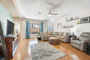 Living room featuring a textured ceiling, a ceiling fan, visible vents, and light wood-style floors