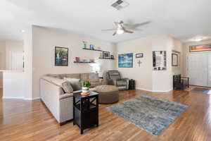 Living area featuring a ceiling fan, visible vents, light wood-style flooring, and baseboards