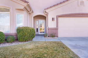 Entrance to property featuring a tile roof, a lawn, an attached garage, and stucco siding