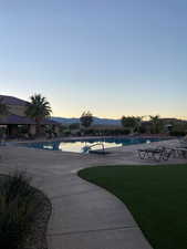 Pool at dusk with a patio area, a community pool, a mountain view, and a lawn