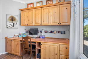 Office area featuring dark wood finished floors, crown molding, and built in study area