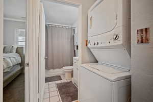 Clothes washing area with light tile patterned floors, a textured wall, stacked washer / dryer, and laundry area