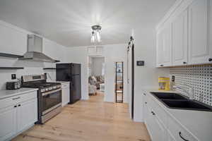 Kitchen with light countertops, wall chimney range hood, gas stove, and freestanding refrigerator