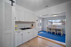 Kitchen featuring light countertops, visible vents, decorative backsplash, white cabinets, and a sink