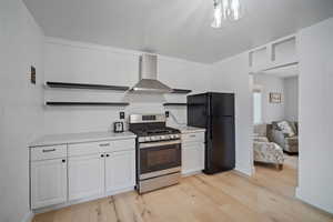 Kitchen with white cabinetry, light countertops, stainless steel gas range, freestanding refrigerator, and wall chimney exhaust hood