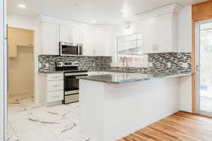 Kitchen featuring marble finish floor, appliances with stainless steel finishes, white cabinetry, dark stone counters, and a peninsula