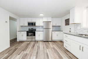 Kitchen featuring white cabinetry, appliances with stainless steel finishes, light stone counters, and light hardwood / wood-style flooring