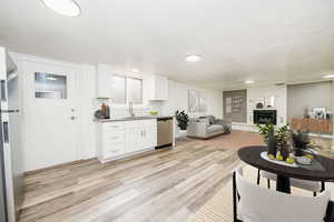 Kitchen with appliances with stainless steel finishes, a fireplace, white cabinetry, sink, and light wood-type flooring