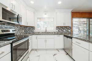 Kitchen featuring marble finish floor, stainless steel appliances, white cabinets, a sink, and light stone countertops