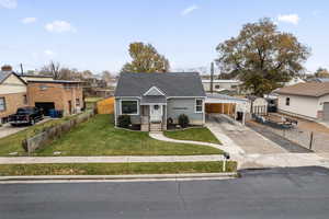 Bungalow-style home featuring an attached carport, fence, concrete driveway, a residential view, and a front lawn