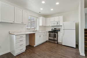 Kitchen with recessed lighting, white appliances, dark wood-style flooring, a sink, and white cabinets