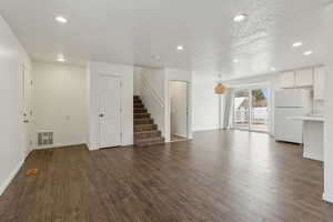 Unfurnished living room with a textured ceiling, recessed lighting, visible vents, stairs, and dark wood-style floors