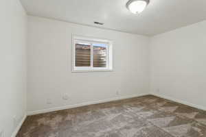 Unfurnished room featuring carpet, a textured ceiling, visible vents, and baseboards